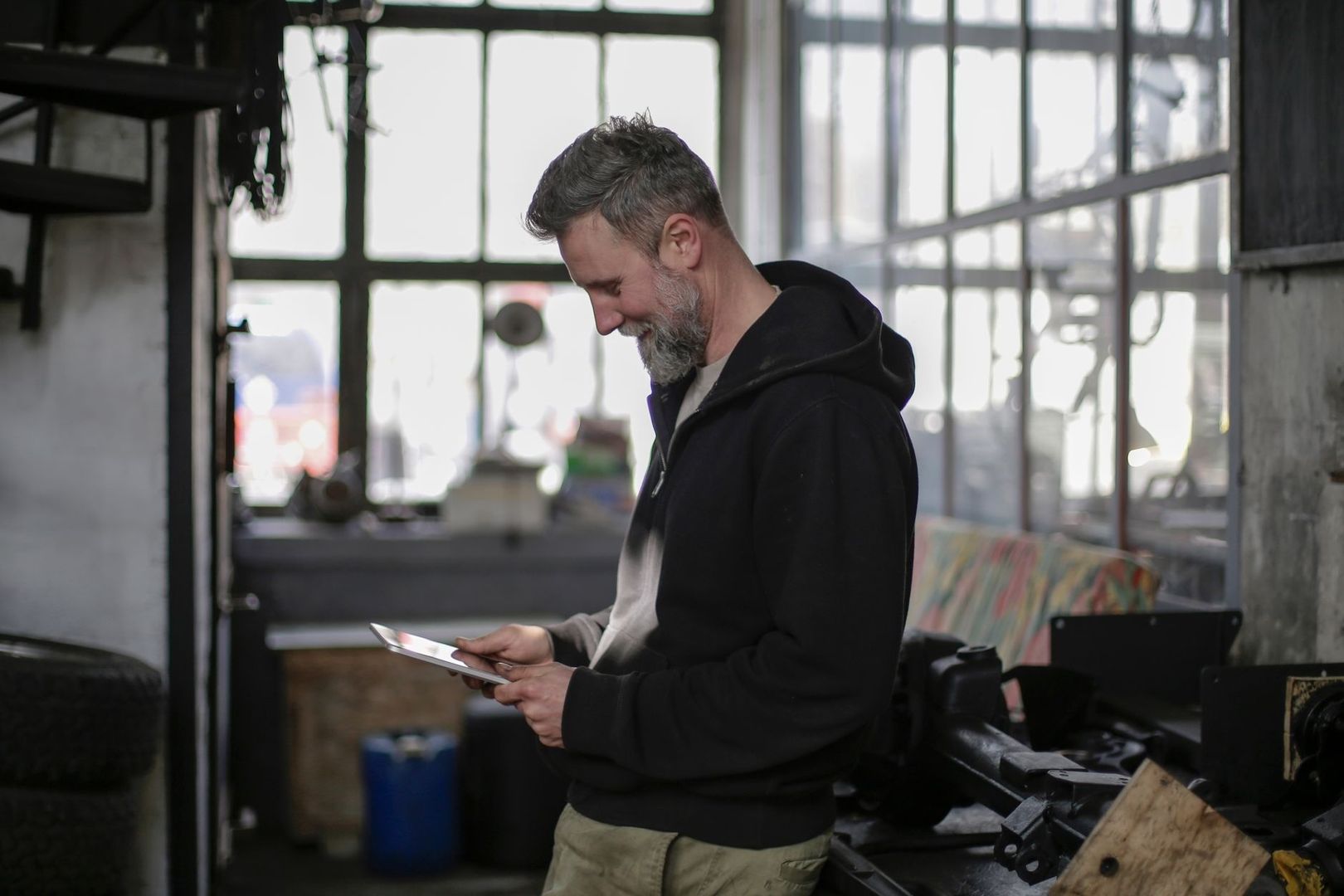 Handwerker prüft ein Tablet in einer Werkstatt mit großen Fenstern